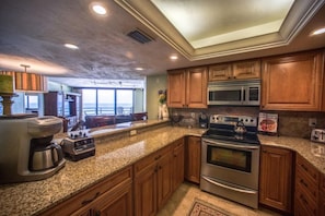 A kitchen with granite countertops, wooden cabinets, stainless steel appliances, and a view to the outside. - #304 Seychelles 3/3 Oceanfront Traffic Free Beach (Daytona Beach Shores)