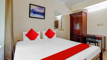 A hotel room with a bed, a desk, a wardrobe, and a painting on the wall.