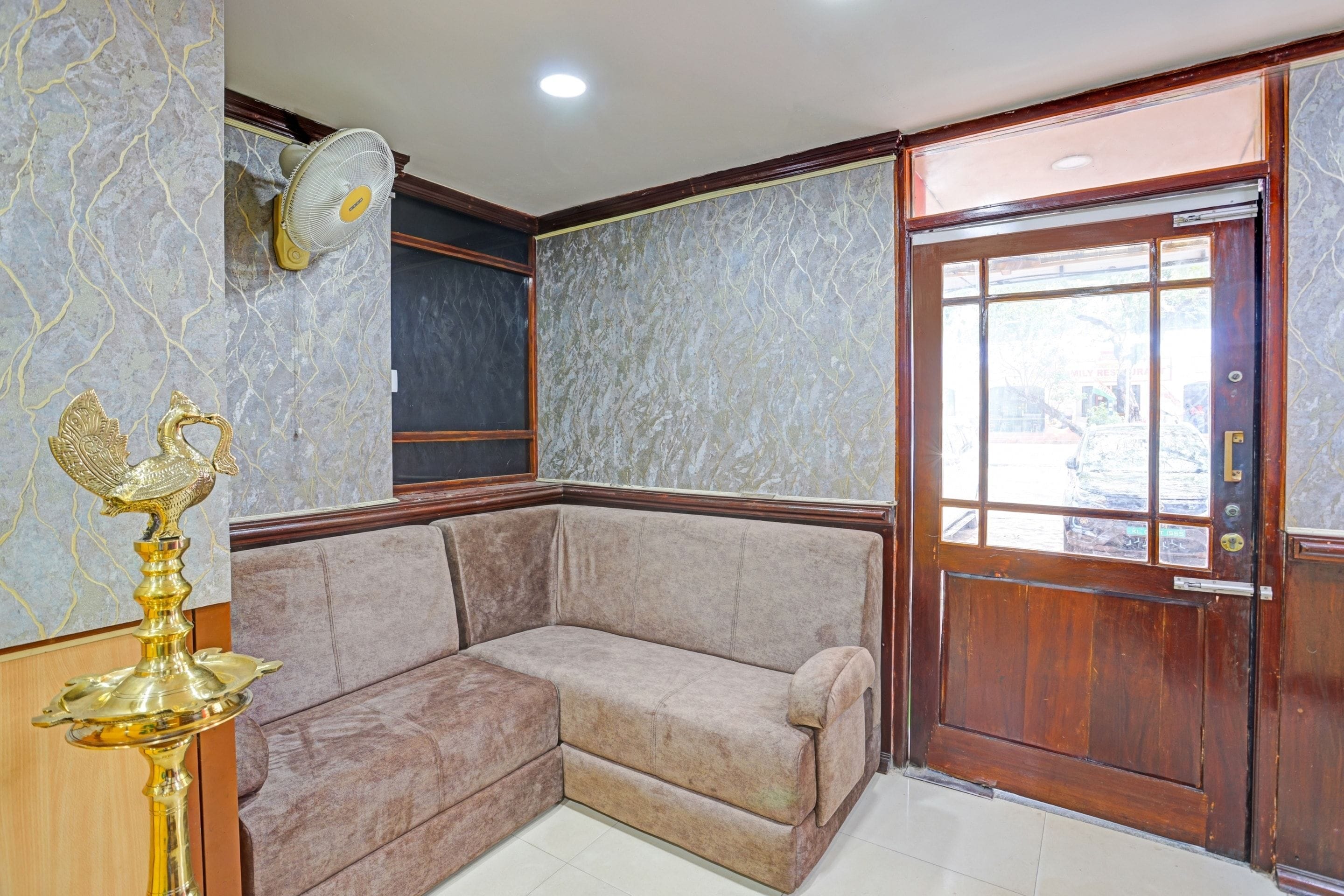 A corner room with a beige sofa, a wooden door, and a marble-patterned wall.