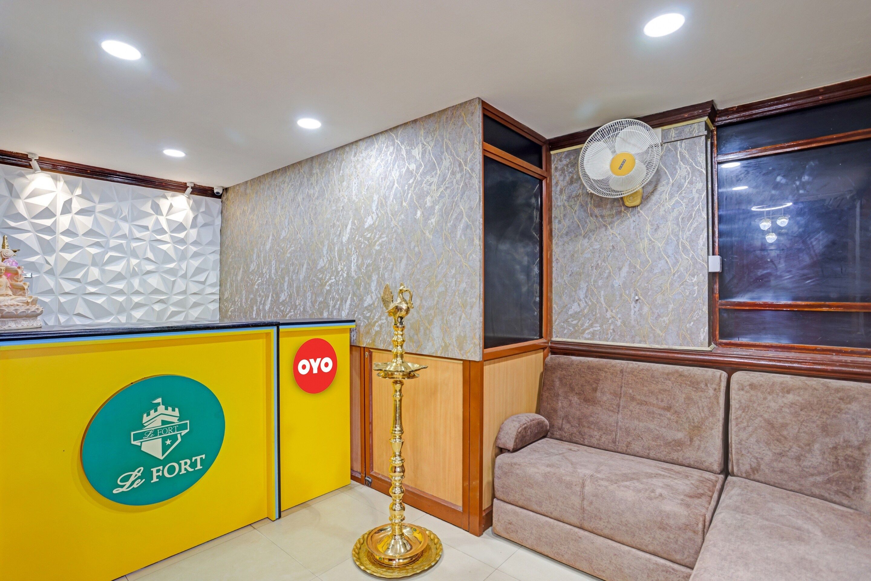 Un espace d’accueil avec un comptoir jaune, un mur décoratif, un ventilateur et un canapé.