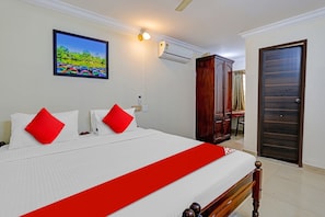 A hotel room with a bed, a painting, an air conditioning unit, and a wooden wardrobe. - Hotel O Le Fort (Thiruvananthapuram)