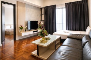 A modern living room with a sofa, a flat-screen TV, a coffee table with a vase, and a bed in the background. - Skyline Service Suite KLCC at The Mews (Kuala Lumpur)