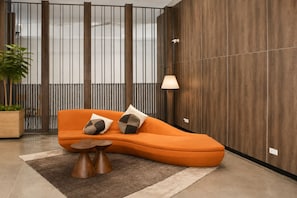 Ein stilvoller Wohnbereich mit einem orangefarbenen, gebogenen Sofa, zwei passenden Kissen, einem kleinen Holztisch und einer Topfpflanze.