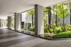 A modern indoor space with a water feature, concrete pillars, and a view of greenery outside. - Skyline Service Suite KLCC at The Mews (Kuala Lumpur)