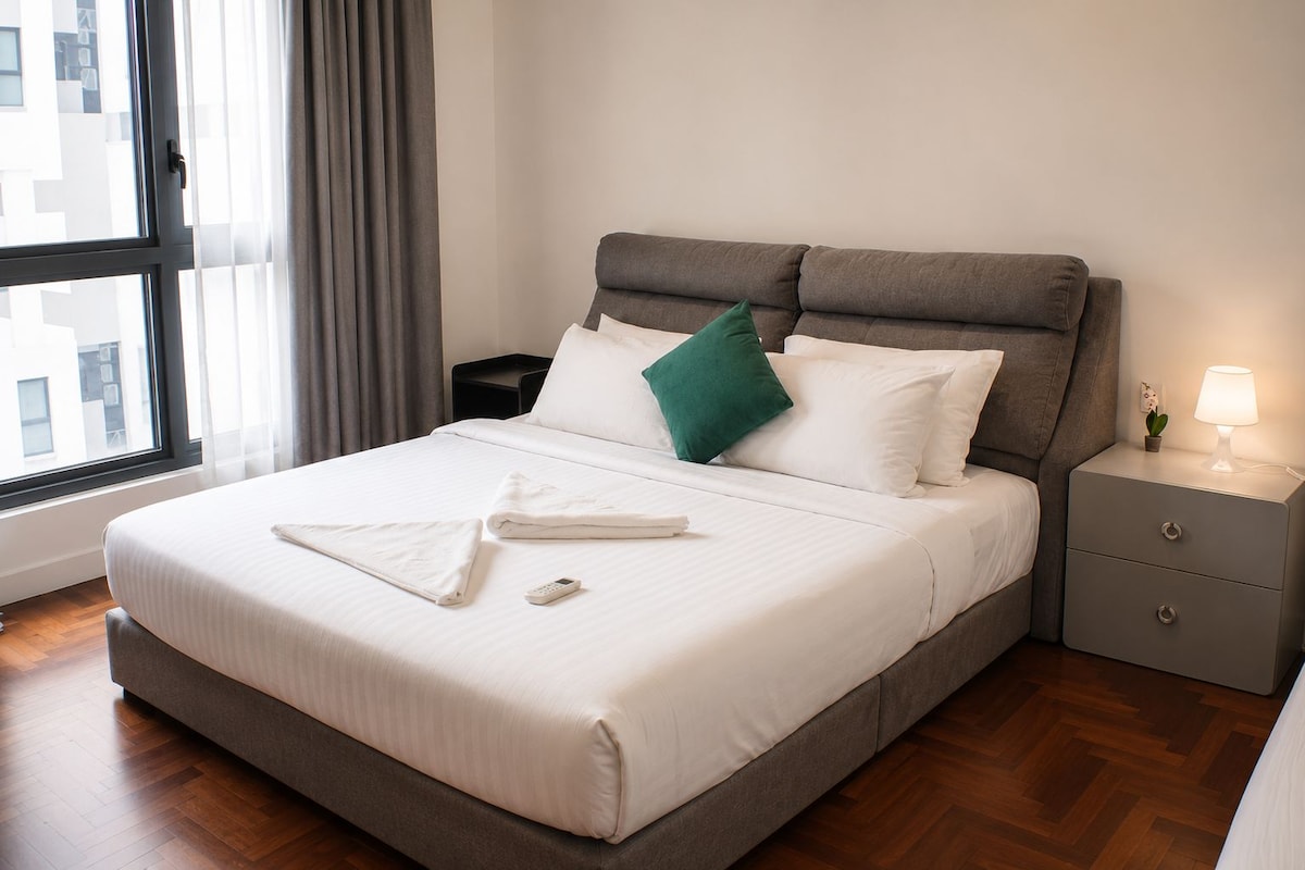 A neatly made bed with white bedding, a remote control, and a green pillow.