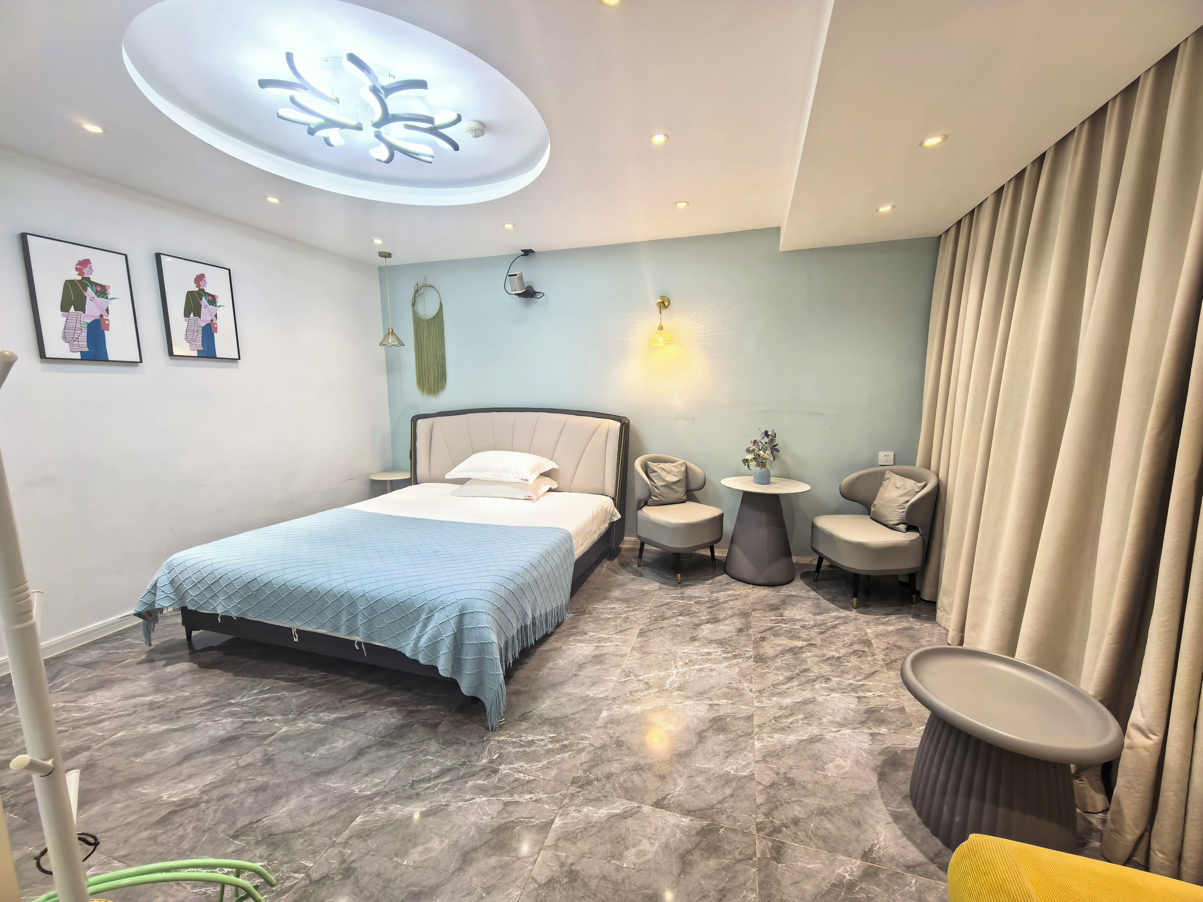A modern bedroom with a bed, two armchairs, a small table, and a ceiling light fixture.