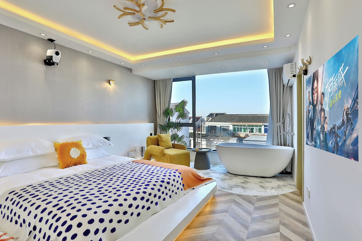 A modern hotel room with a large bed, a bathtub, and a view of the city.