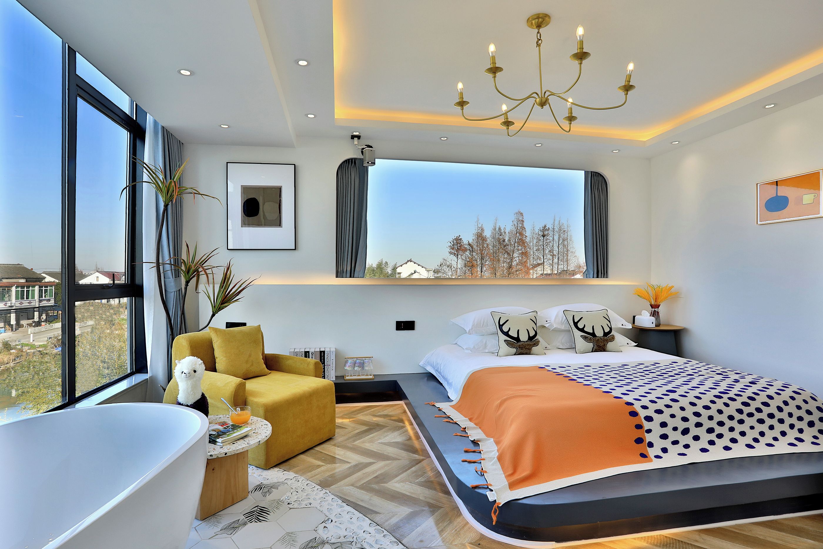 A modern bedroom with a large bed, a sitting area, a bathtub, and a view of the city.