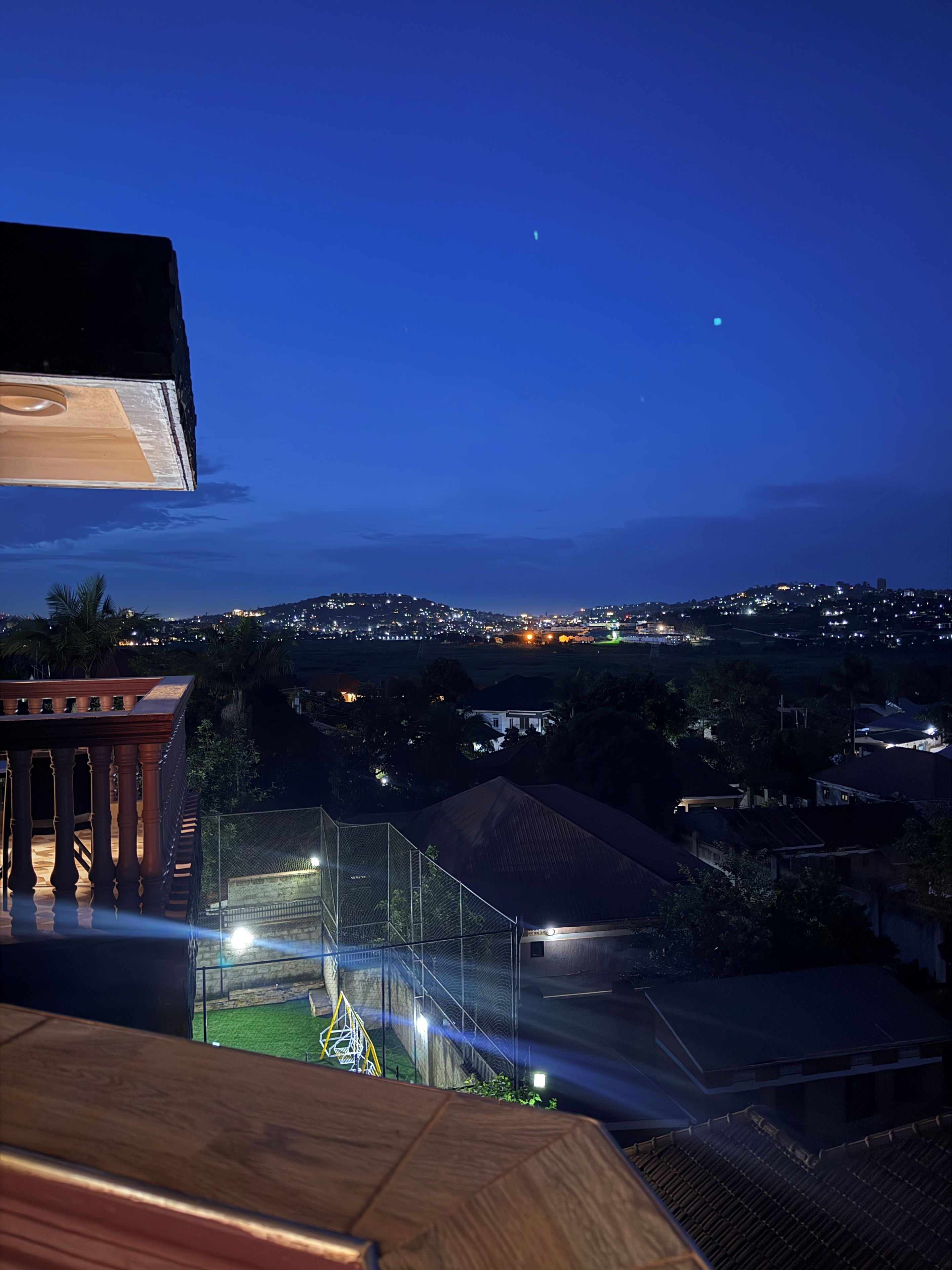 Vista nocturna d'una zona residencial amb un balcó que fa a l'ampli d'un camp esportiu.
