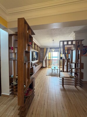 A spacious living room with wooden flooring, built-in wooden shelving, a large window with curtains, and a view of the outdoors. - Lake view 2-bedroom apartment with power backup in vibrant Kampala neighborhood (Kampala)