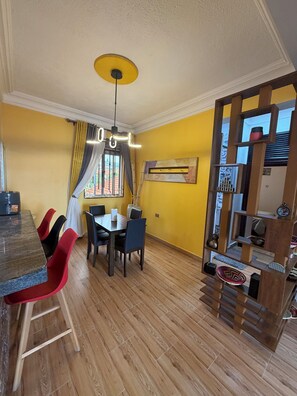 A dining area with a wooden floor, a table with chairs, a hanging light fixture, and a window with curtains. - Lake view 2-bedroom apartment with power backup in vibrant Kampala neighborhood (Kampala)