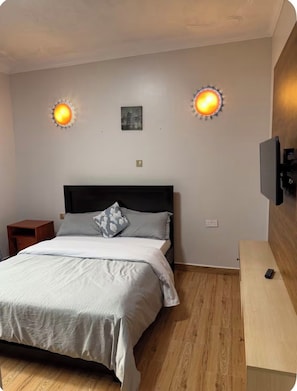 A bedroom with a bed, a nightstand, a wall-mounted TV, and two wall sconces. - Lake view 2-bedroom apartment with power backup in vibrant Kampala neighborhood (Kampala)