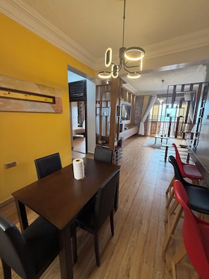 Ein Essbereich mit Holztisch und Stühlen, einer Hängelampe und Blick in den angrenzenden Wohnraum.