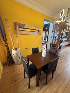 A dining area with a wooden table and chairs, a vase with bamboo, and a wall-mounted light fixture. - Lake view 2-bedroom apartment with power backup in vibrant Kampala neighborhood (Kampala)