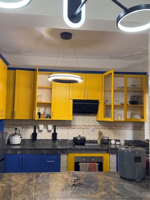 A kitchen with yellow cabinets, a black countertop, and a modern pendant light. - Lake view 2-bedroom apartment with power backup in vibrant Kampala neighborhood (Kampala)