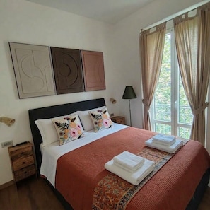 A neatly made bed with a red blanket, pillows with floral patterns, and a folded towel on the bed. - "Il Mondo Nuovo," a modern and cozy apartment in Porta Nuova. (Milano)