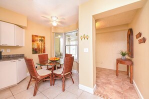 A kitchen with white cabinets, a glass-top dining table, wicker chairs, and a ceiling fan. - Towers 4104 in Ponce Inlet, FL (Ponce Inlet)