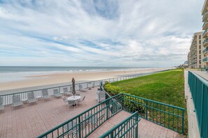A beachside balcony with a view of the ocean, a grassy area, and a building in the background. - Towers 4104 in Ponce Inlet, FL (Ponce Inlet)
