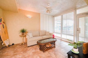 A living room with a striped sofa, a glass coffee table, and a ceiling fan. - Towers 4104 in Ponce Inlet, FL (Ponce Inlet)