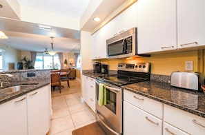 A modern kitchen with granite countertops, stainless steel appliances, and a dining area with a table and chairs. - Towers 4104 in Ponce Inlet, FL (Ponce Inlet)