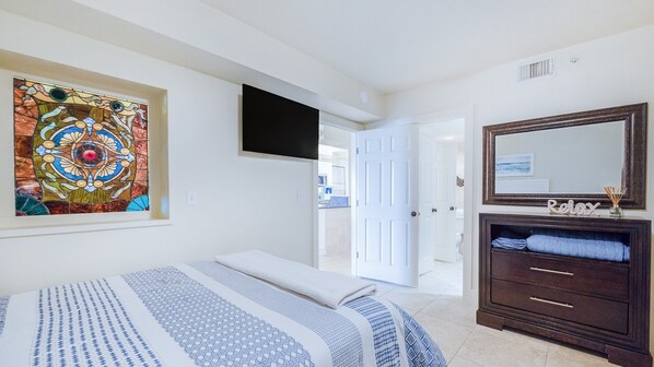 A bedroom with a bed, a dresser, a television, and a door leading to another room. - #7306 Towers 8&9 Oceanfront 2/2 condo (Ponce Inlet)