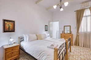 A bedroom with two beds, a nightstand, a dresser, a mirror, and a chandelier. - 2BR Maltese Townhouse in Bormla close to harbour (Cospicua)