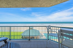 A balcony with a view of the beach, a pool, and a covered area with a table and chairs. - Towers at Ponce Inlet 1206 (Ponce Inlet)