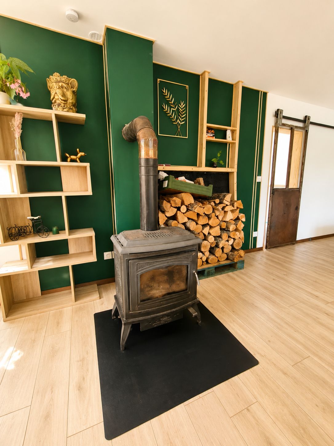Une pièce dotée d’un poêle à bois, d’étagères en bois et d’un mur d’accent vert.