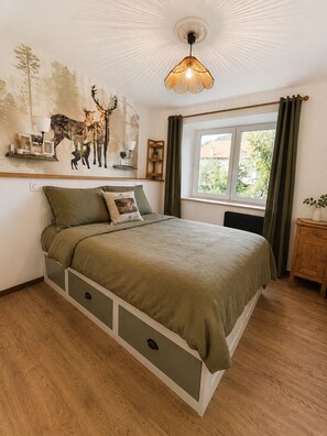 Un dormitorio con cama, estante en la pared, ventana con cortinas y lámpara de techo.