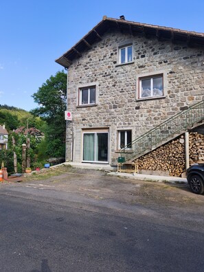 Un bâtiment en pierre avec un escalier menant à une terrasse en bois, une porte et une fenêtre donnant sur un paysage agréable.