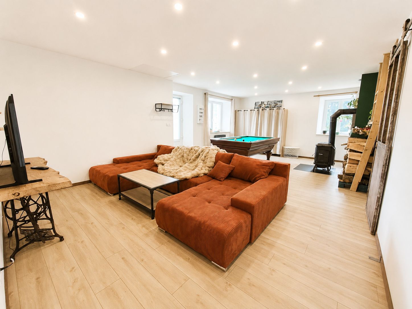 Una sala de estar con una mesa de billar, un sofá, un televisor y una chimenea.