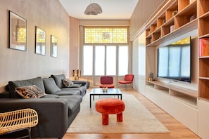 A modern living room with a grey sofa, red chairs, a coffee table, and a TV on a wooden shelf. - Luxueux Logement Design 4 ch Clim (Lille)