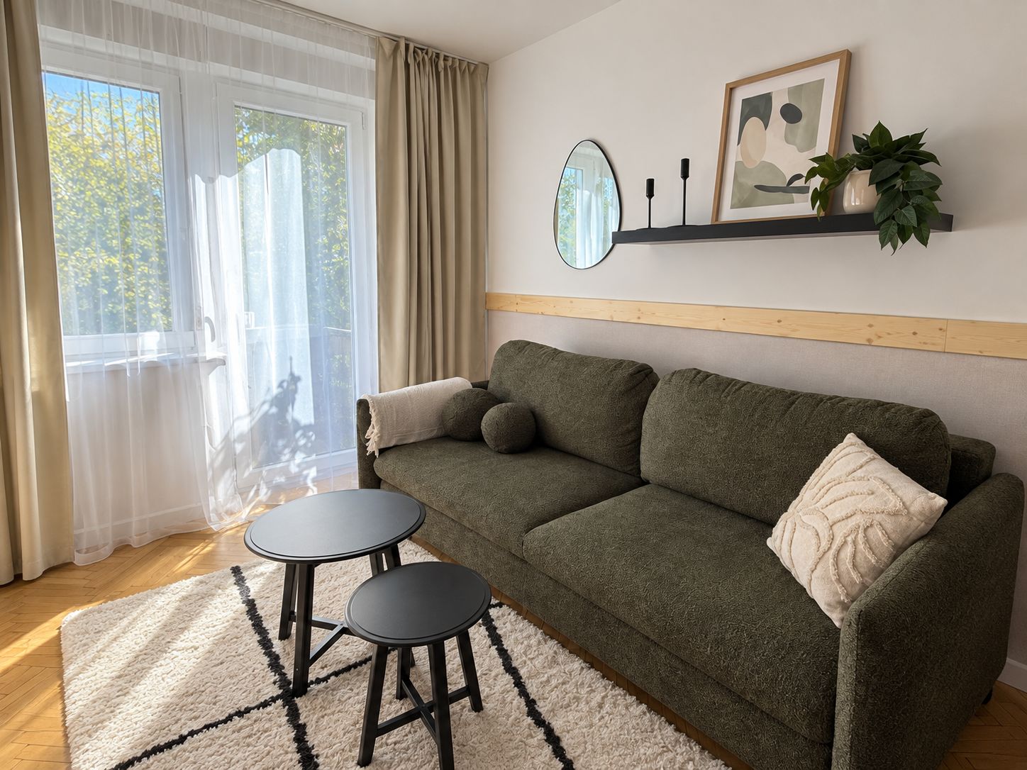A cozy living room with a sofa, two small tables, a mirror, and a shelf with decorative items.