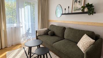 A cozy living room with a sofa, two small tables, a mirror, and a shelf with decorative items.