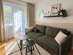 A cozy living room with a sofa, two small tables, a mirror, and a shelf with decorative items. - Family Apartment with Balcony (Gdańsk)
