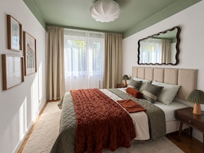 A bedroom with a large bed, a nightstand, a mirror, and a window with curtains. - Family Apartment with Balcony (Gdańsk)