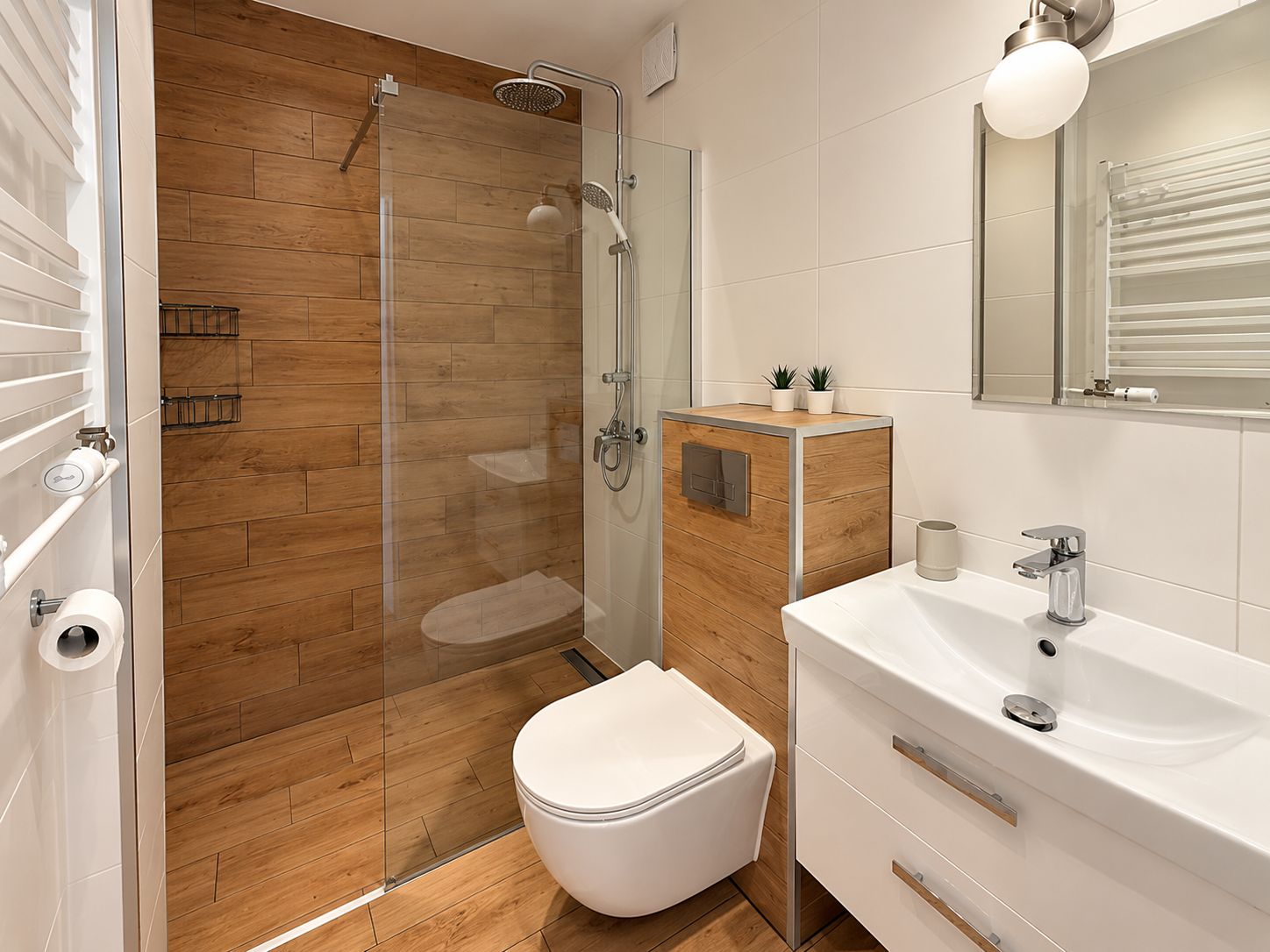 A modern bathroom with a glass shower enclosure, a toilet, a sink with a mirror, and a small cabinet with plants.