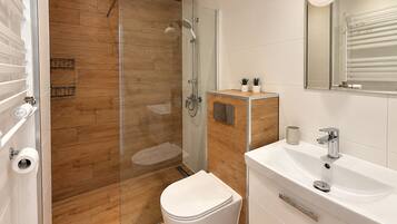 A modern bathroom with a glass shower enclosure, a toilet, a sink with a mirror, and a small cabinet with plants.
