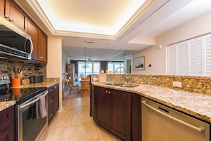 A kitchen with dark wood cabinets, granite countertops, stainless steel appliances, and a view to the dining area. - #6410 Towers Oceanview 2/2 Condo (Ponce Inlet)