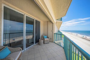 Ein Balkon mit Blick auf den Strand, eine Korbsitzgruppe und ein kleiner Tisch mit Kissen.