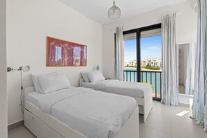 Ein Hotelzimmer mit zwei Betten, einem großen Fenster mit Vorhängen, einer Deckenleuchte und einem Gemälde an der Wand.