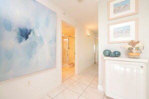 Een gang met een groot abstract schilderij, een glazen douchecabine en een kast met decoratieve objecten.