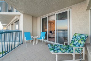 Een balkon met een zithoek, inclusief stoelen en een bank, en een schuifdeur naar een binnenruimte met een bank en een tafel.