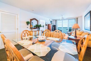 A dining area with a glass table, wooden chairs, and a buffet bowl. - #802 Towers 10 Oceanfront 2/2 Condo. (Daytona Beach Shores)