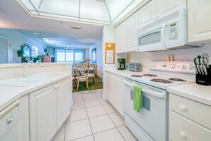A modern kitchen with white cabinets, a microwave, stove, and a dining area with a table and chairs. - #802 Towers 10 Oceanfront 2/2 Condo. (Daytona Beach Shores)