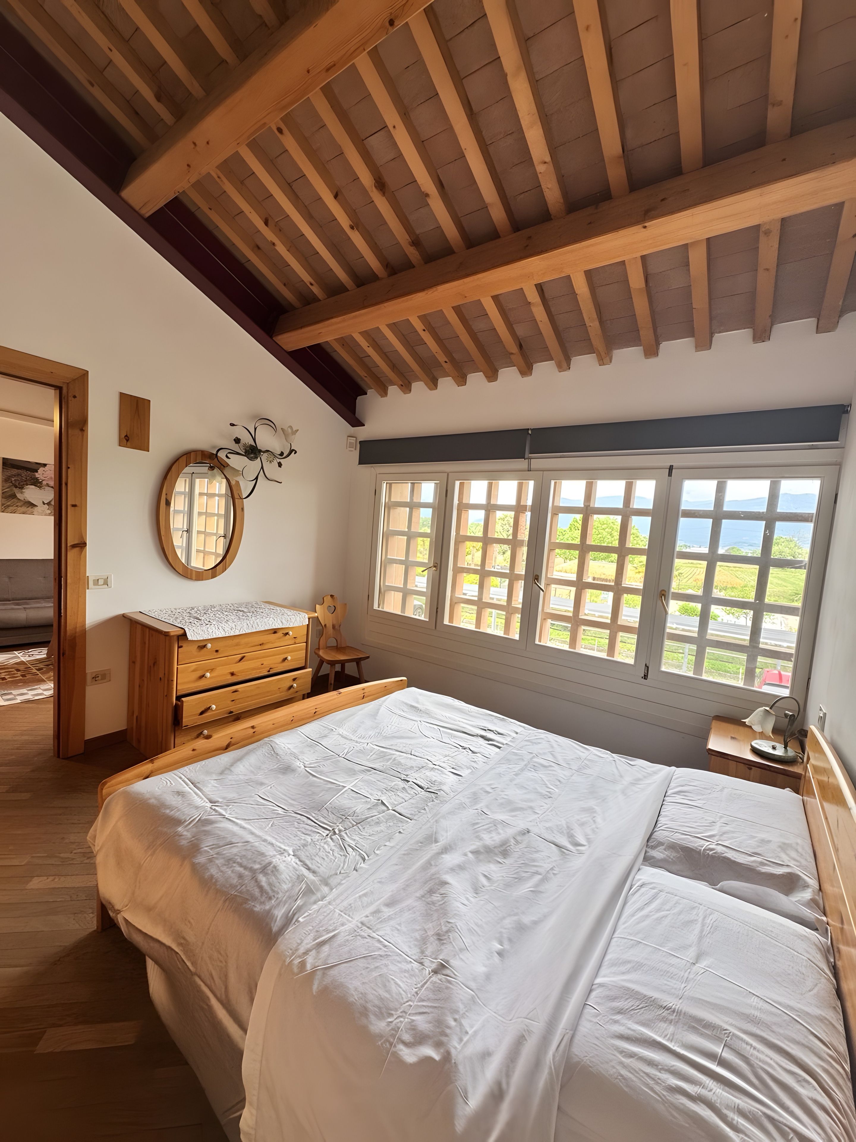 Une chambre avec un plafond en bois, un grand lit, une commode, une chaise et une fenêtre donnant sur un beau paysage.