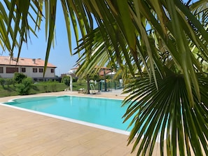 A swimming pool with a tiled deck, surrounded by greenery and a clear sky. - Apartment 'Nonna Giuseppina - Bilocale' with Shared Pool, Wi-Fi and Air Conditioning (Romano d'Ezzelino)