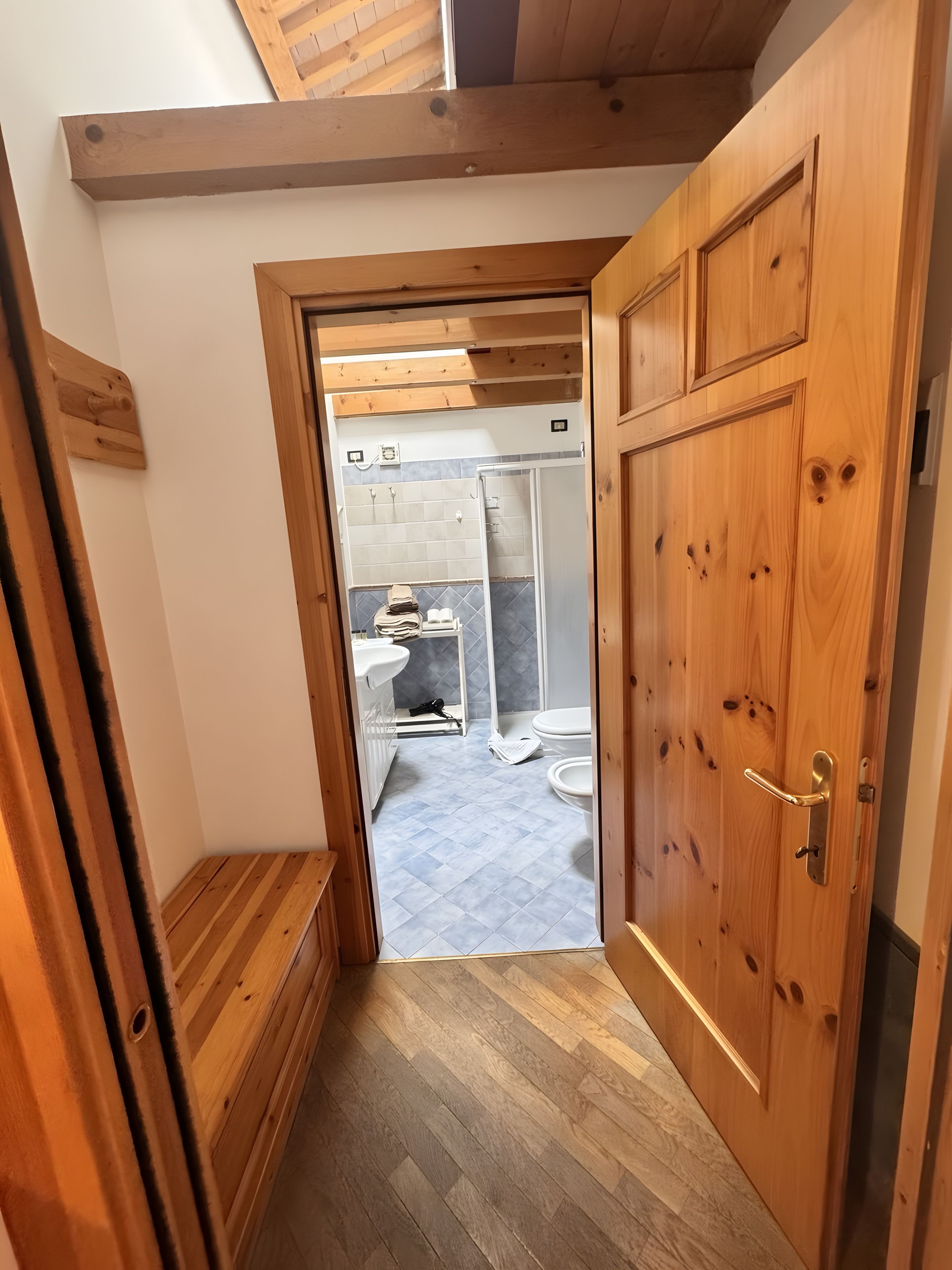 Puerta de madera que da a un baño con ducha, inodoro y lavabo.