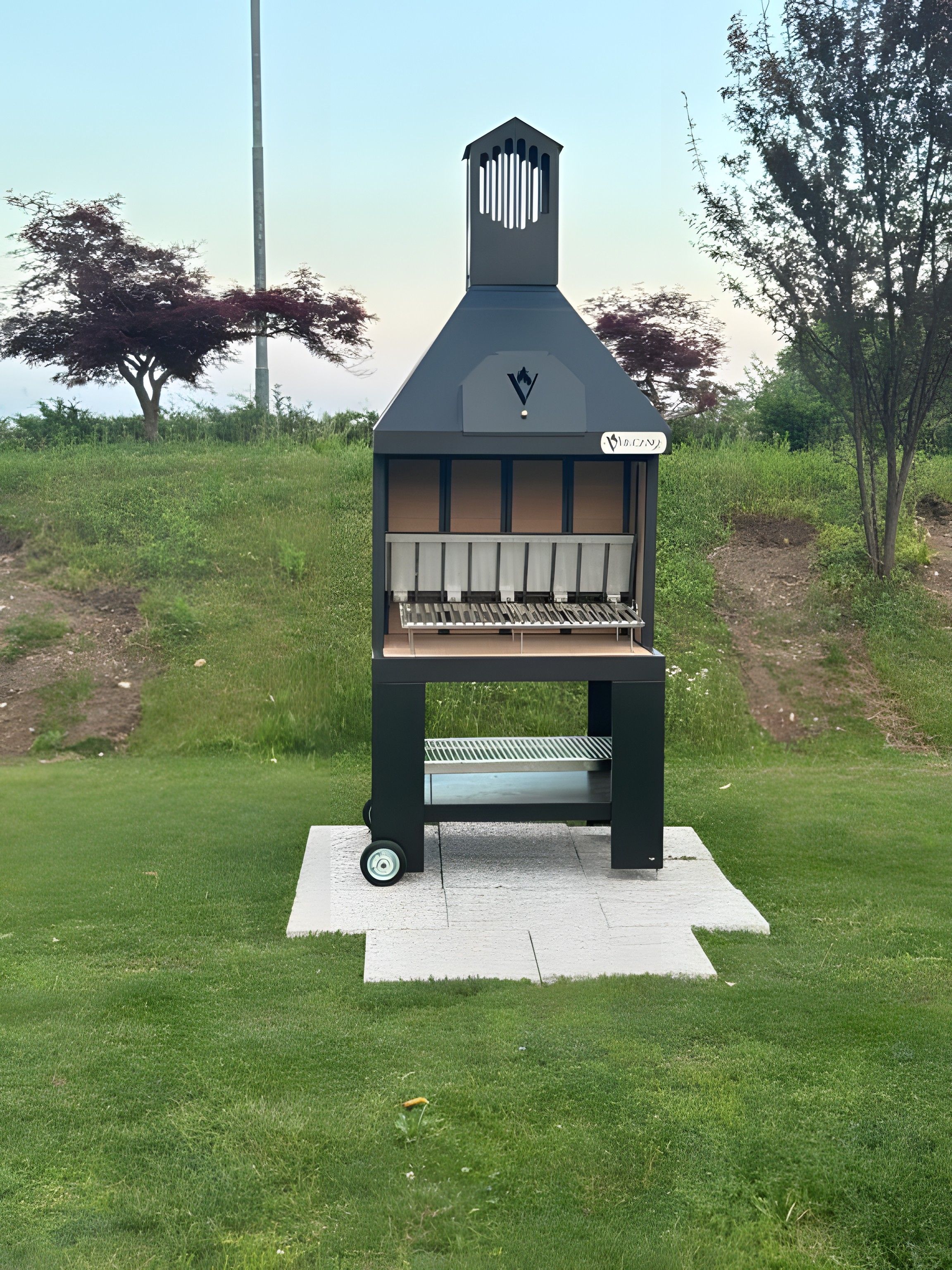 A portable barbecue grill with a chimney, wheels, and a label in a grassy outdoor area.