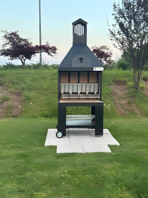 Una griglia barbecue portatile con un camino, ruote e un’etichetta in una zona verde all'aperto.